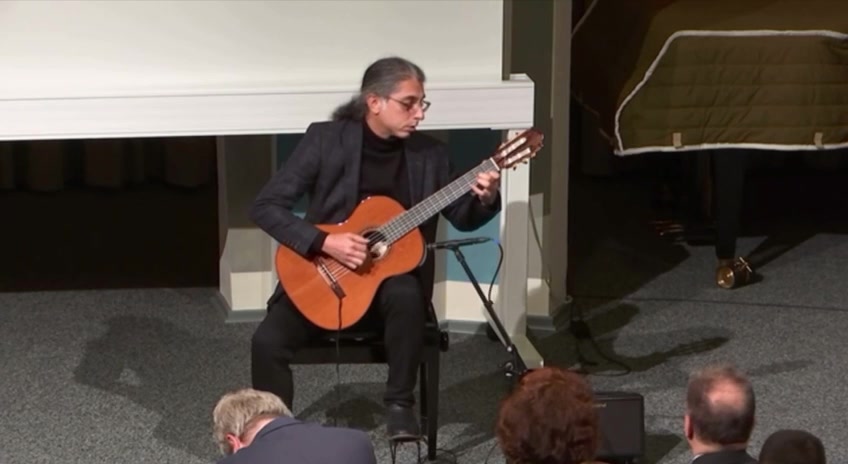 Mohammadali Masjedi seated, playing classical guitar on a concert stage